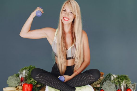 Woman lifting a small dumbbell while surrounded by fresh vegetables, embodying health and fitness.